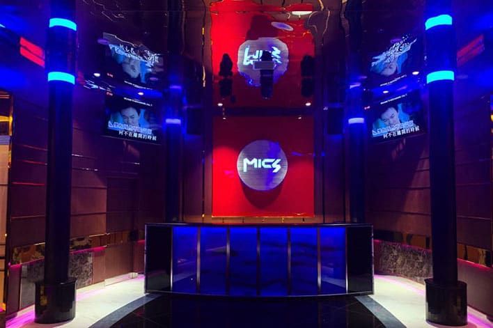 MICS Karaoke with a prominent "MICS" logo on a red-lit wall, reflective surfaces, blue accent lights, and TV screens displaying Asian text.